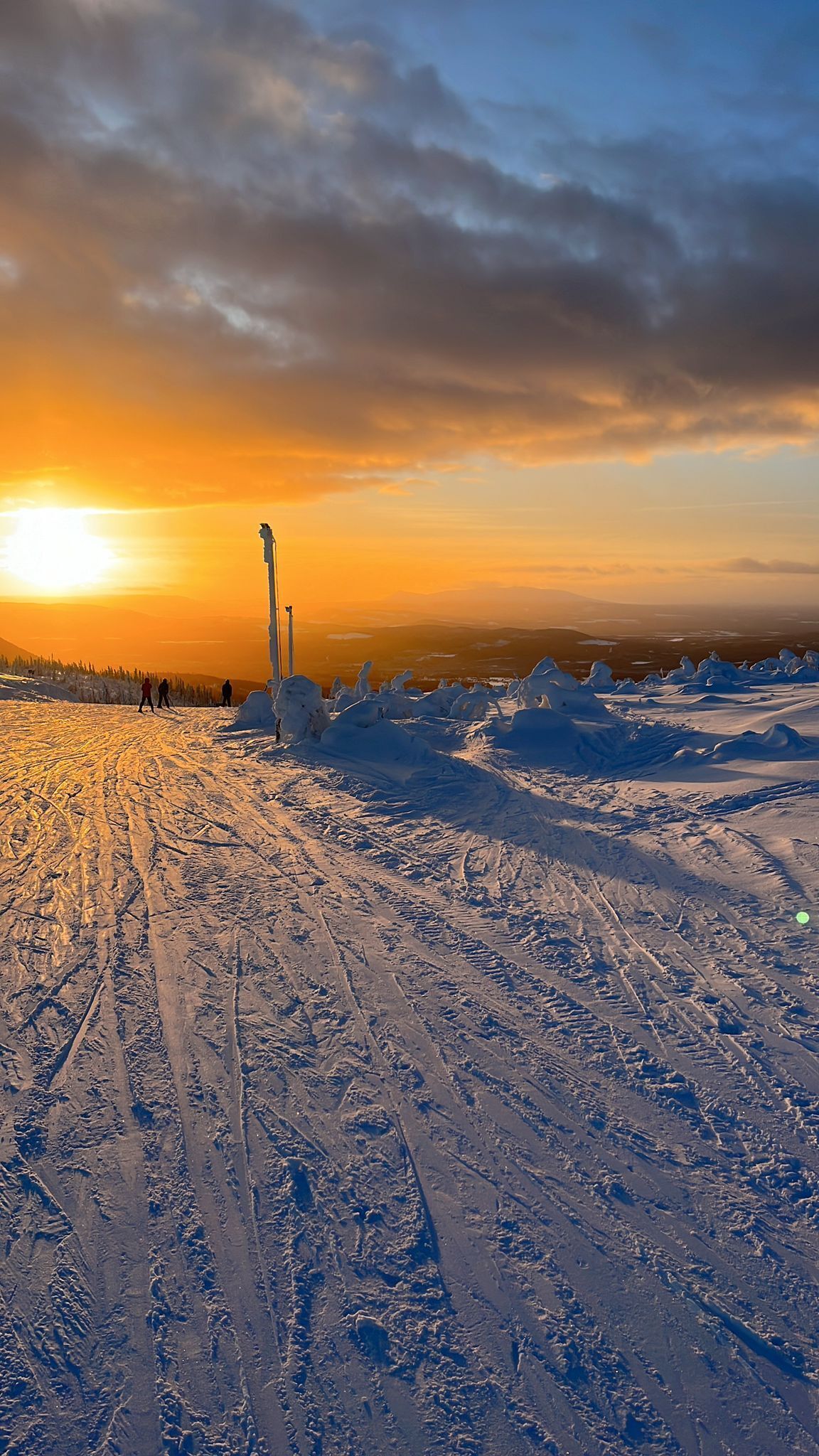 Eine verschneite Landschaft bei Sonnenuntergang, eine hohe Struktur und Spuren im Schnee.