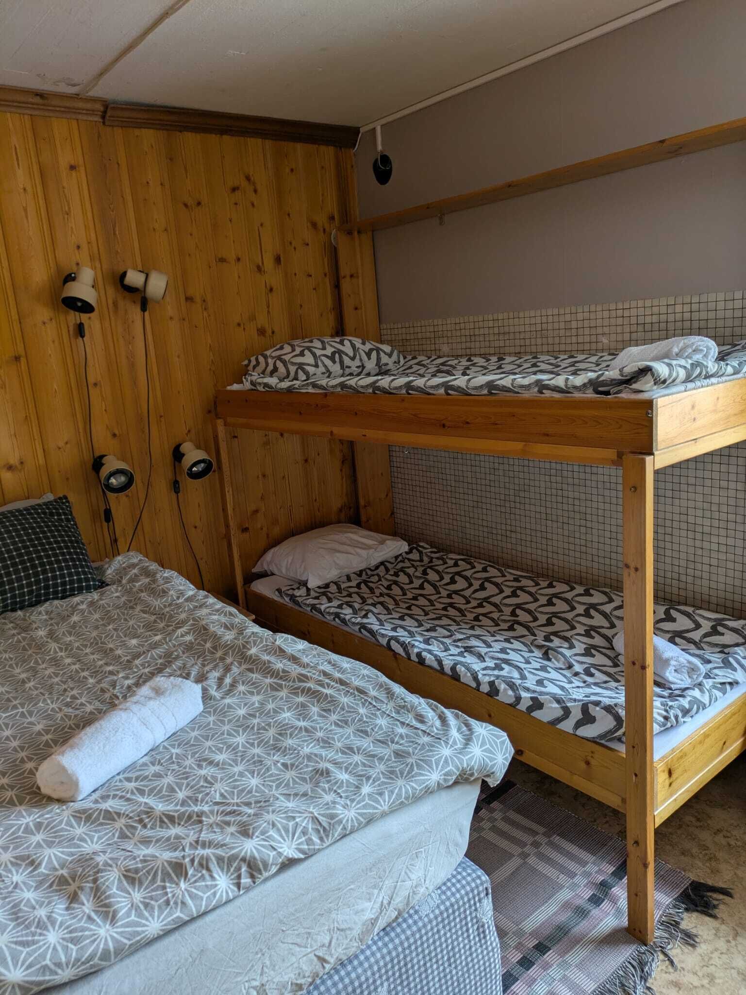 Una cama literera con ropa de cama estampada, un armario de madera y una lámpara fijada a la pared.