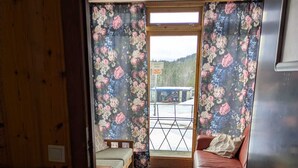 Een kamer met een bed, een bank, een houten vloer, een raam met bloemen gordijnen en uitzicht op een treinstation.