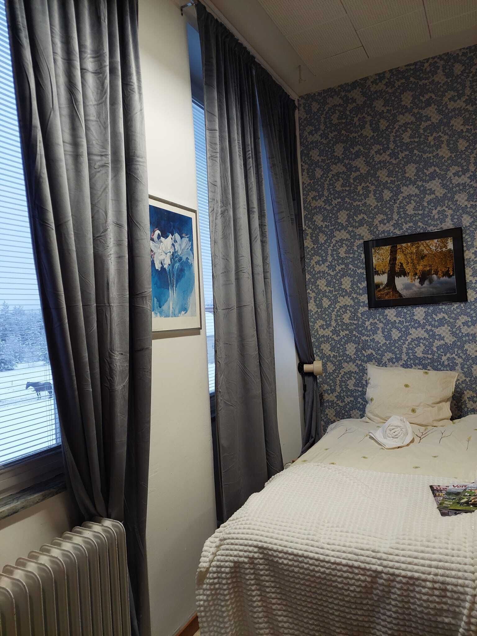 Un dormitorio con una cama, un radiador, cortinas y dos cuadros en la pared.