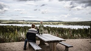 A wooden picnic table with benches, overlooking a lake with forested hills in the background. - Hotel Nederhögen Vildmarkscenter (Rätan)