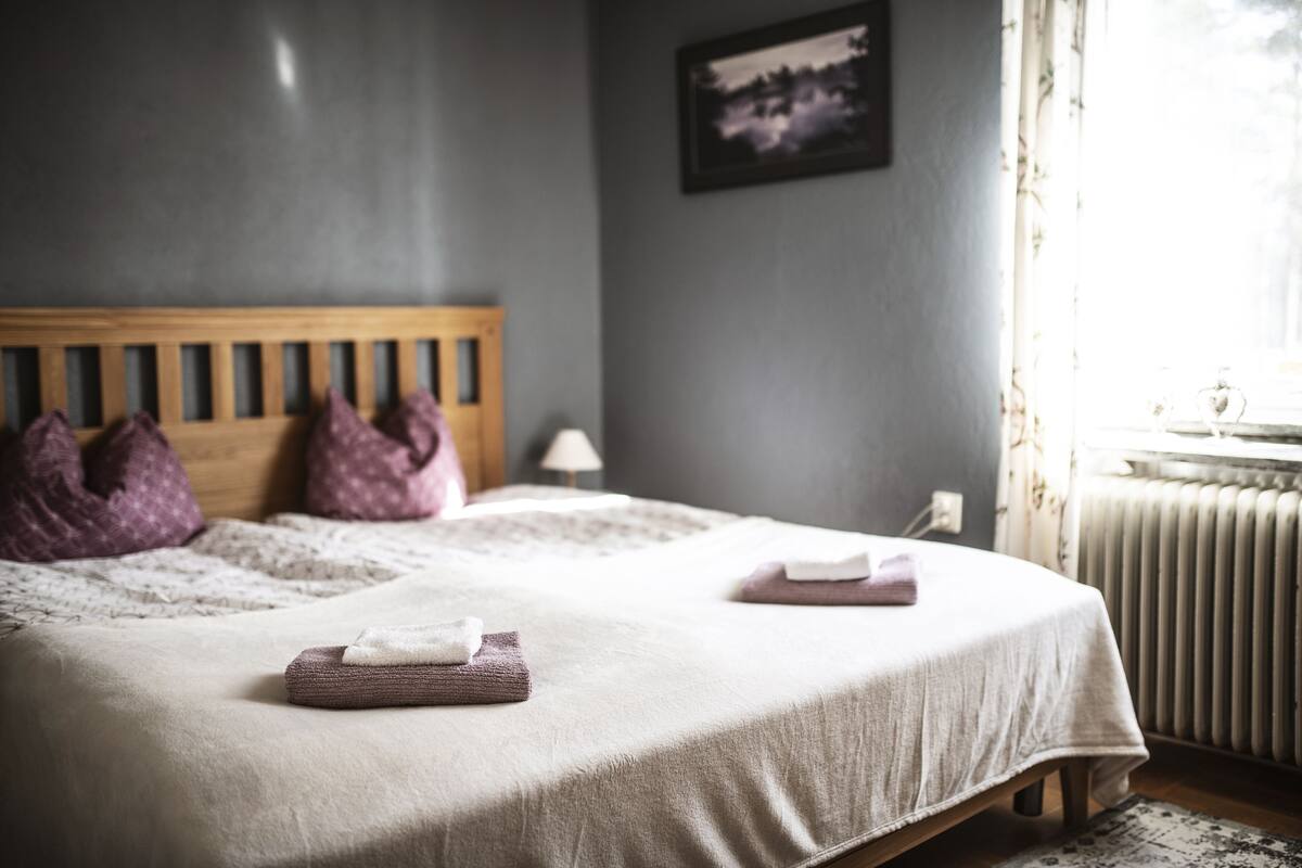 Una cama bien hecha con cabecera de madera, dos almohadas y toallas dobladas.