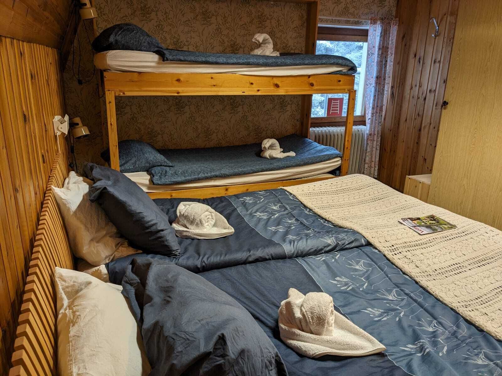 Une chambre avec un lit superposé, une tête de lit en bois, une fenêtre donnant sur un beau paysage et une table avec un magazine.