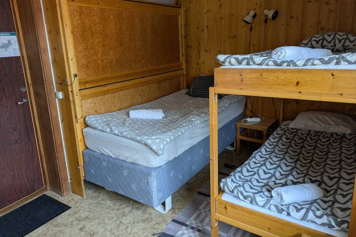 Habitación con literas de madera, una cama individual y una mesita de noche pequeña.