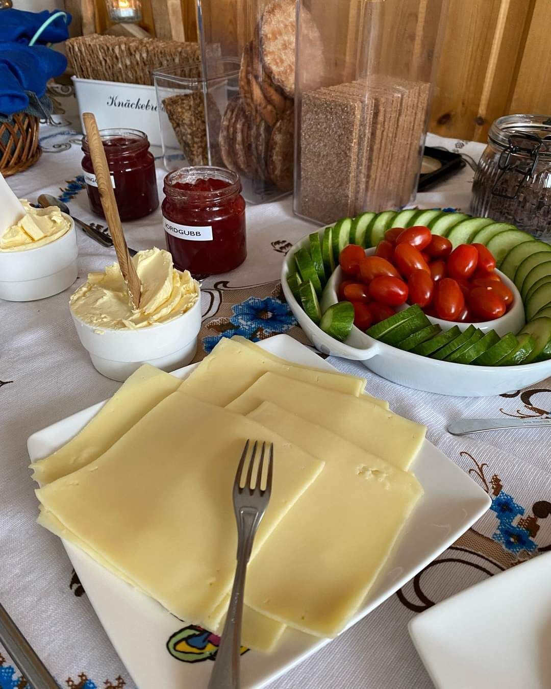 A table with cheese, butter, jam, and vegetables.