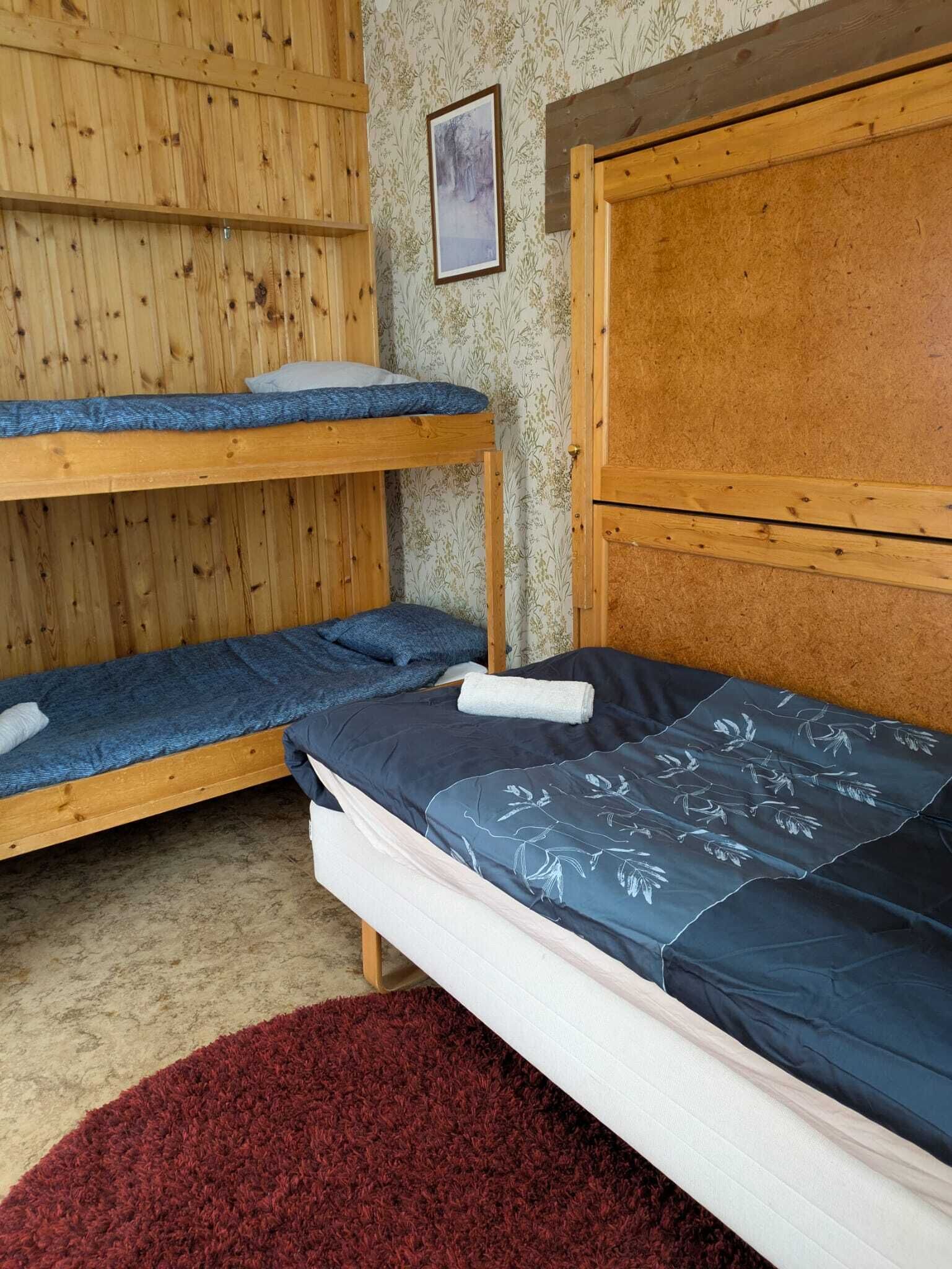 Habitación con literas, cabecera de madera, una cama individual con colcha floral y una alfombra roja en el suelo.