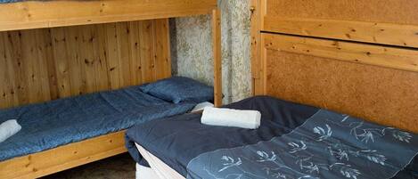 Habitación con literas, cabecera de madera, una cama individual con colcha floral y una alfombra roja en el suelo.
