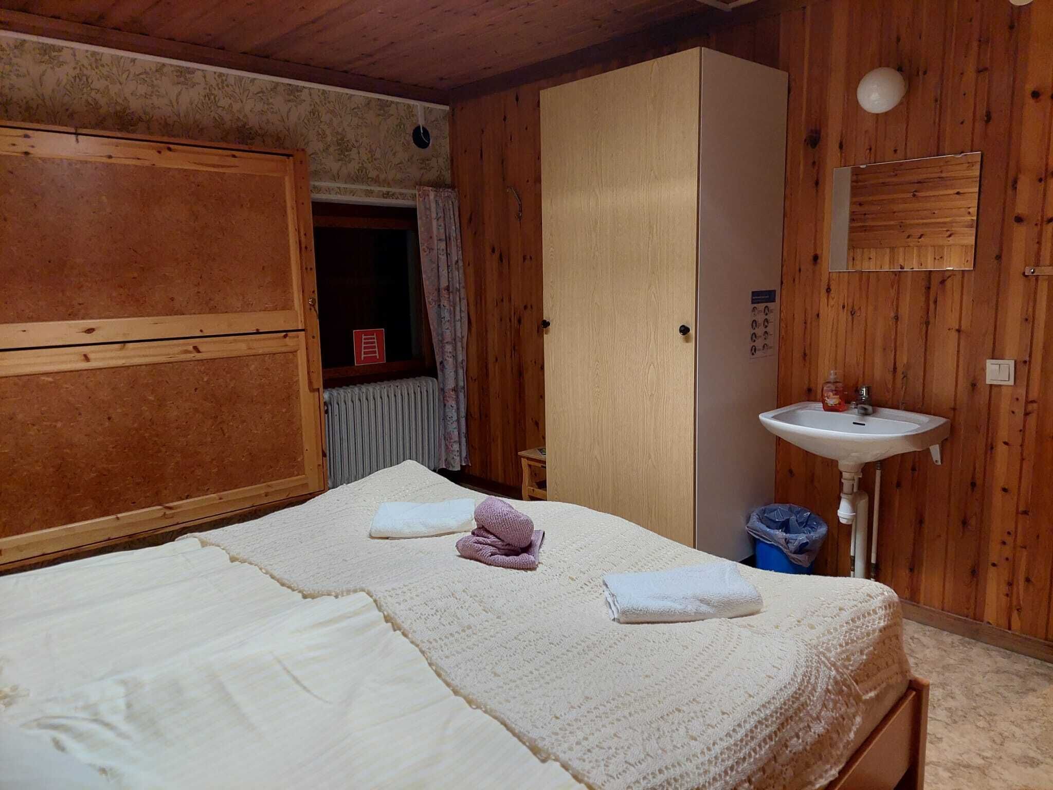 A room with a bed, a wardrobe, a sink, and a window with curtains.