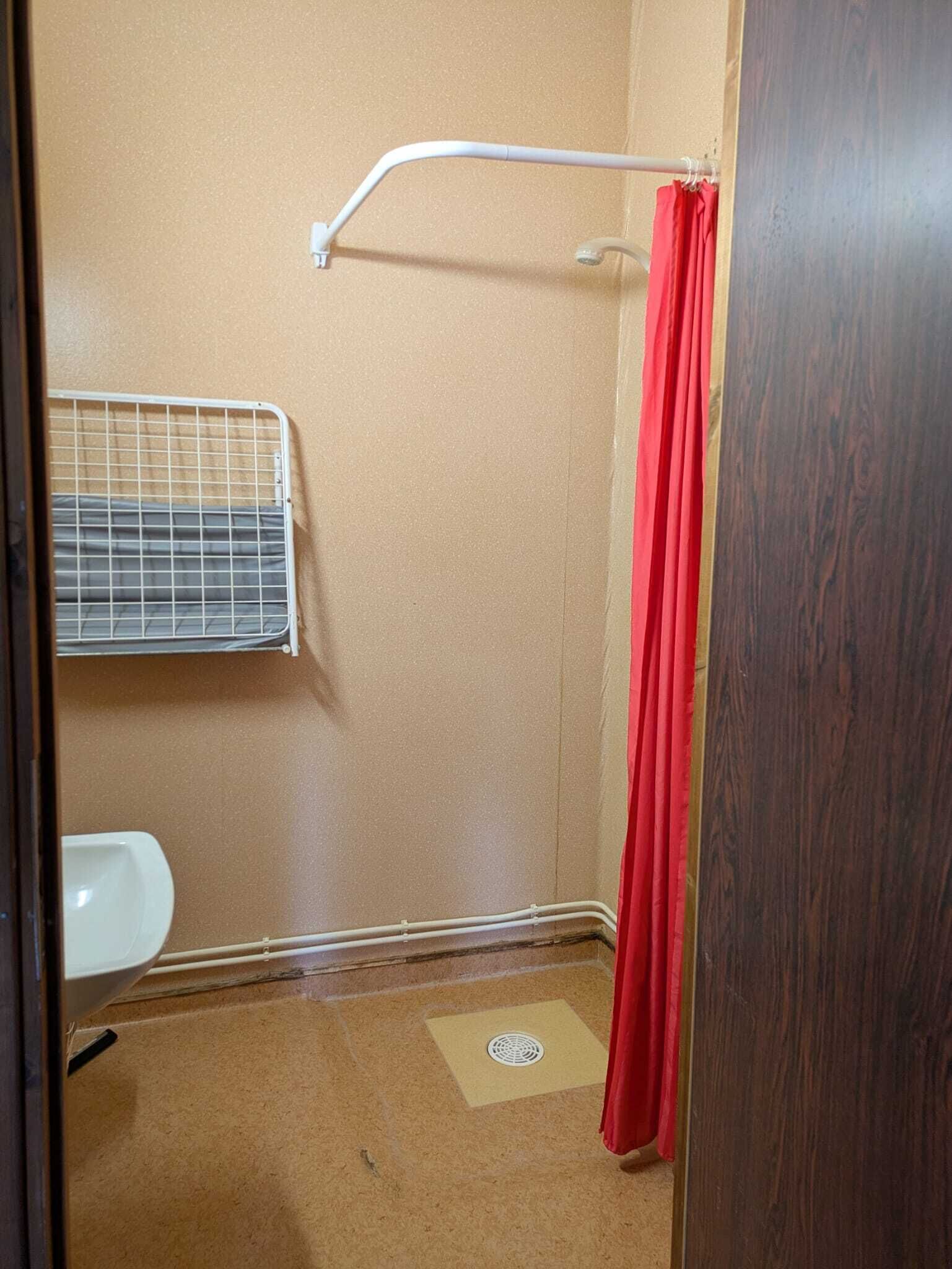Un baño pequeño y cerrado con ducha, inodoro y estante metálico.