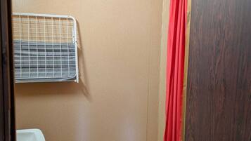 Un baño pequeño y cerrado con ducha, inodoro y estante metálico.