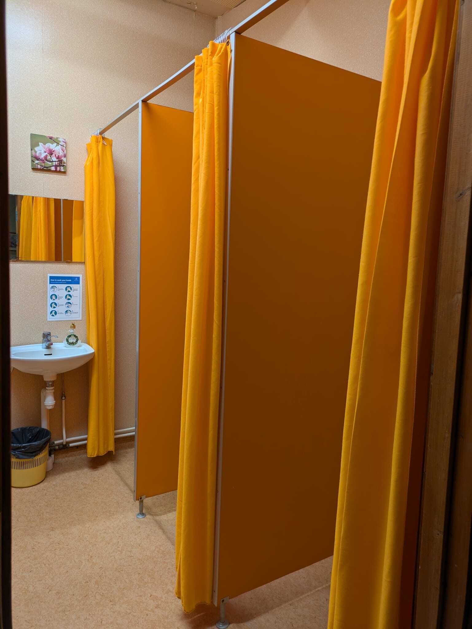 A bathroom with yellow curtains, a sink, and a trash bin.