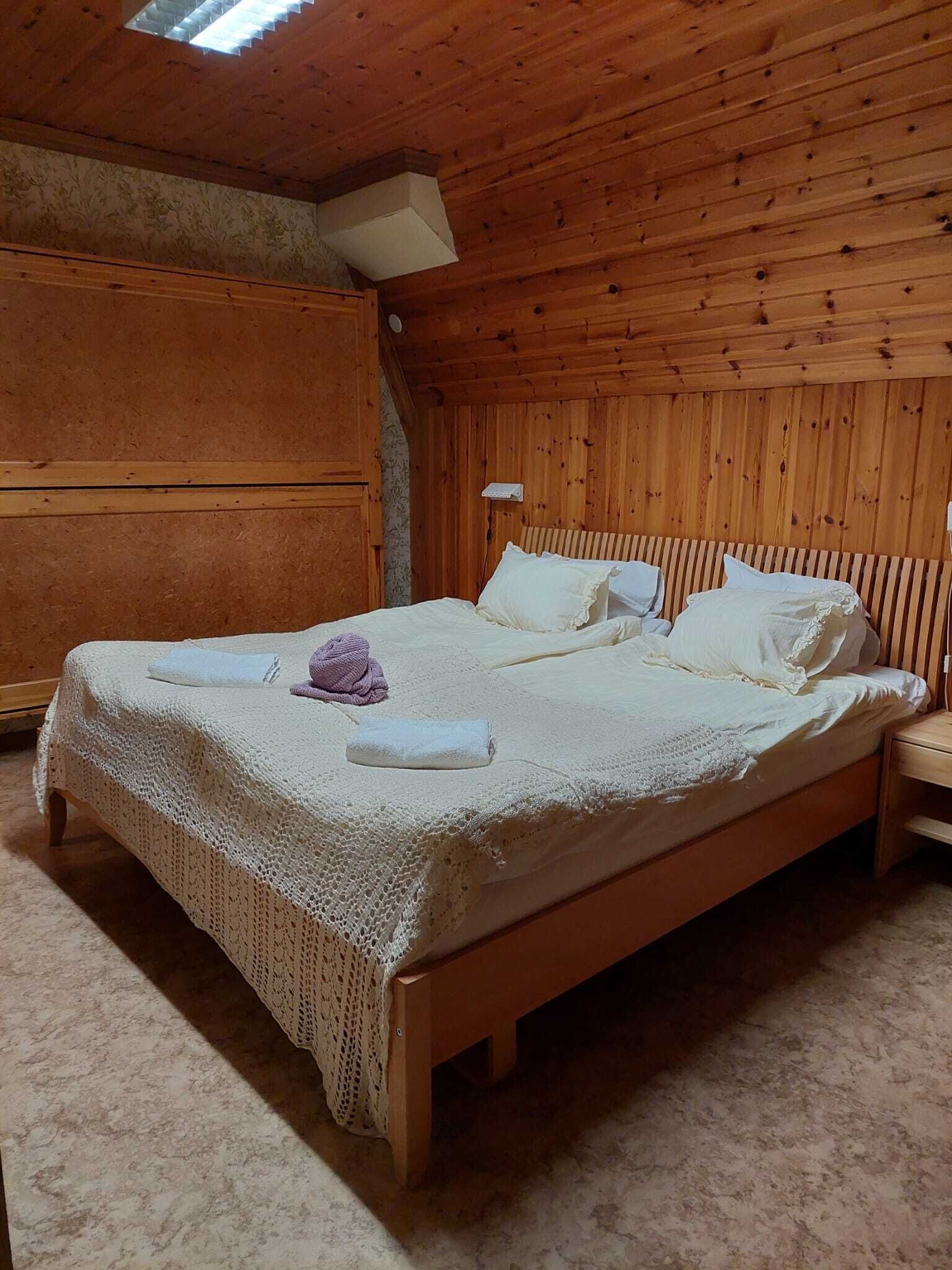 Une chambre à coucher aux murs lambrissés, avec un grand lit, une table de chevet et une lucarne.