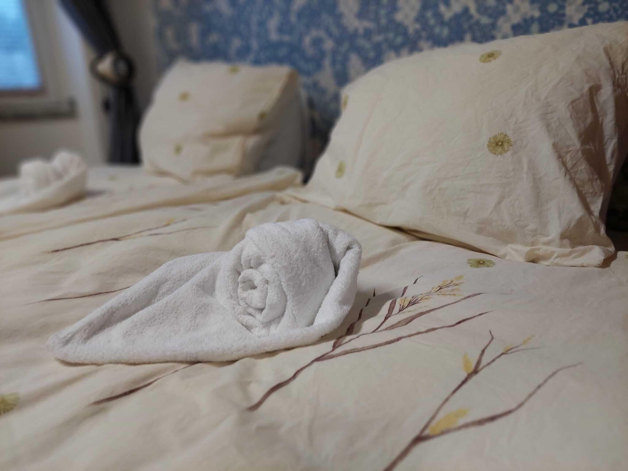 A bed with a white blanket and pillows, a floral pattern on the wall, and a window with curtains.