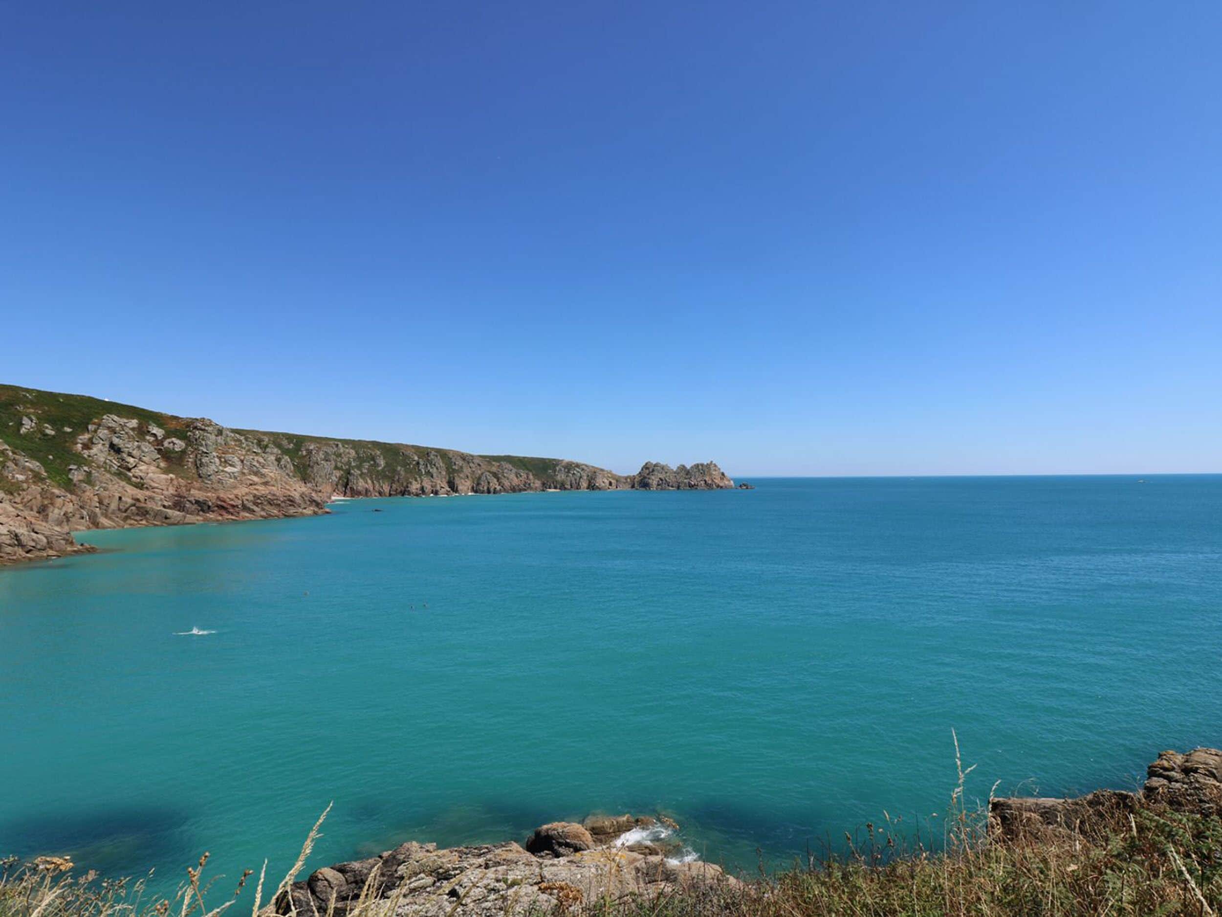 A coastal landscape with clear turquoise waters, rocky cliffs, and a small boat in the distance.