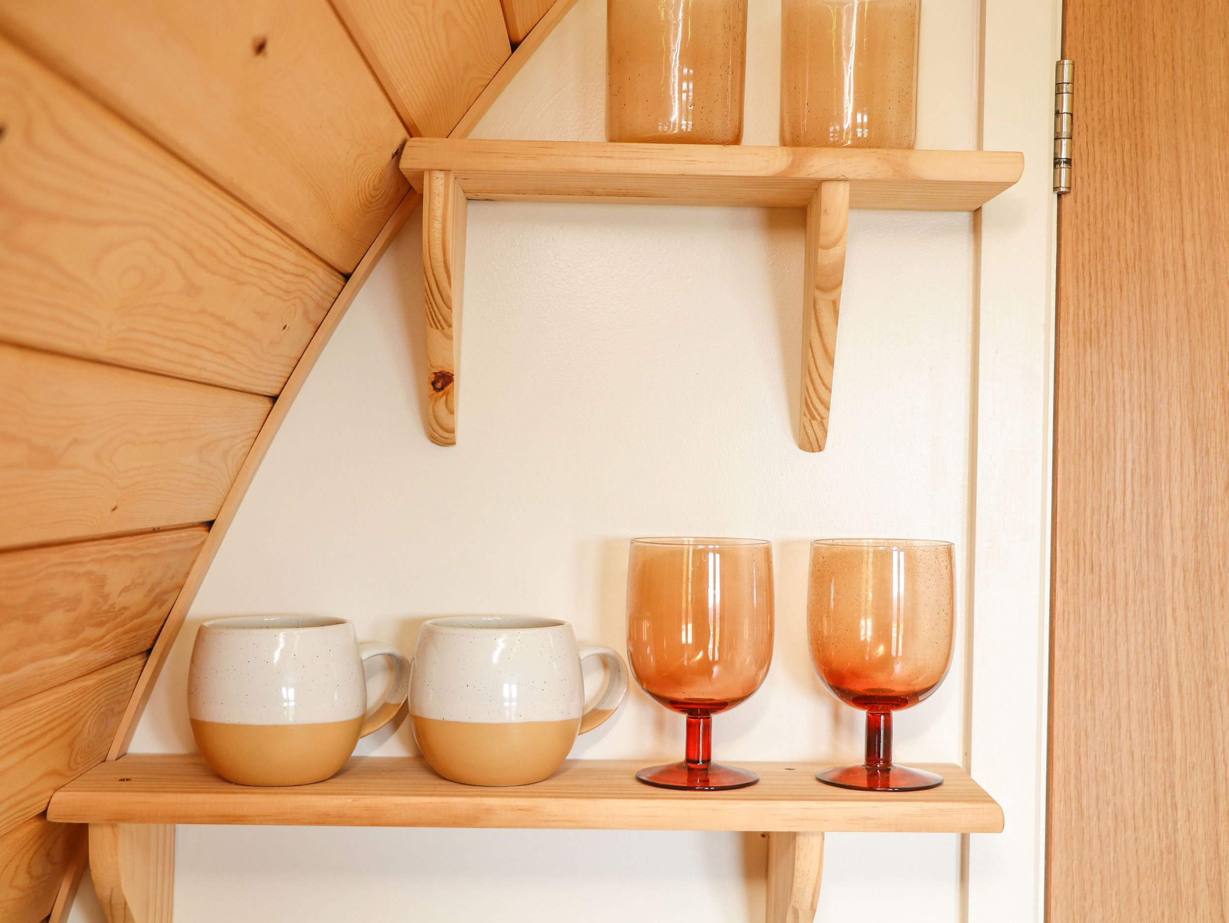 Una estantería de madera con tres tazas de cerámica y dos vasos de vidrio.