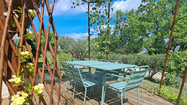 A wooden deck with a metal table and chairs, surrounded by greenery and a metal trellis with flowers. - Country house in a beautiful natural setting, in the heart of the Gard department (Sauzet)