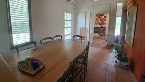 A dining area with a wooden table, chairs, and a tray with glasses. There is a window with blinds, a door leading to another room, and a potted plant. - Country house in a beautiful natural setting, in the heart of the Gard department (Sauzet)