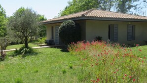 A single-story house with a tiled roof, a small garden with red flowers, and a tree to the left. - Country house in a beautiful natural setting, in the heart of the Gard department (Sauzet)