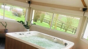 Un baño moderno con una bañera de madera, suelo de baldosas negras y ventanas amplias que ofrecen vistas a un paisaje verde.