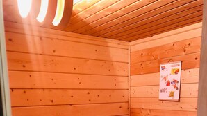 Una sauna con paredes y bancos de madera, una toalla sobre un banco y un cartel con símbolos de sauna.