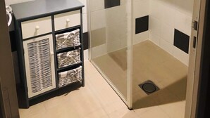 Un baño pequeño con ducha, espejo y un mueble de almacenamiento con cestas.