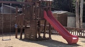 A wooden play structure with a red slide and a small house-like building.