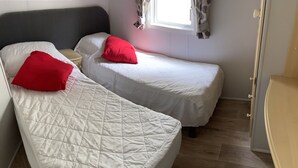 A room with two single beds, each with a red pillow, a bedside table, and a window with curtains.