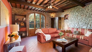A cozy living room with a stone wall, wooden beams, and a large arched window. - Podere Belvedere 6, Emma Villas (Montevarchi)
