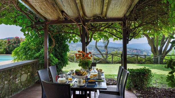 An outdoor dining area with a table set for breakfast, surrounded by greenery and overlooking a scenic landscape. - Podere Belvedere 6, Emma Villas (Montevarchi)