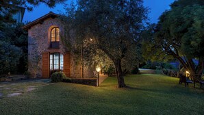 A stone building with an arched window and a door, surrounded by a well-maintained lawn and trees. - Podere Belvedere 6, Emma Villas (Montevarchi)