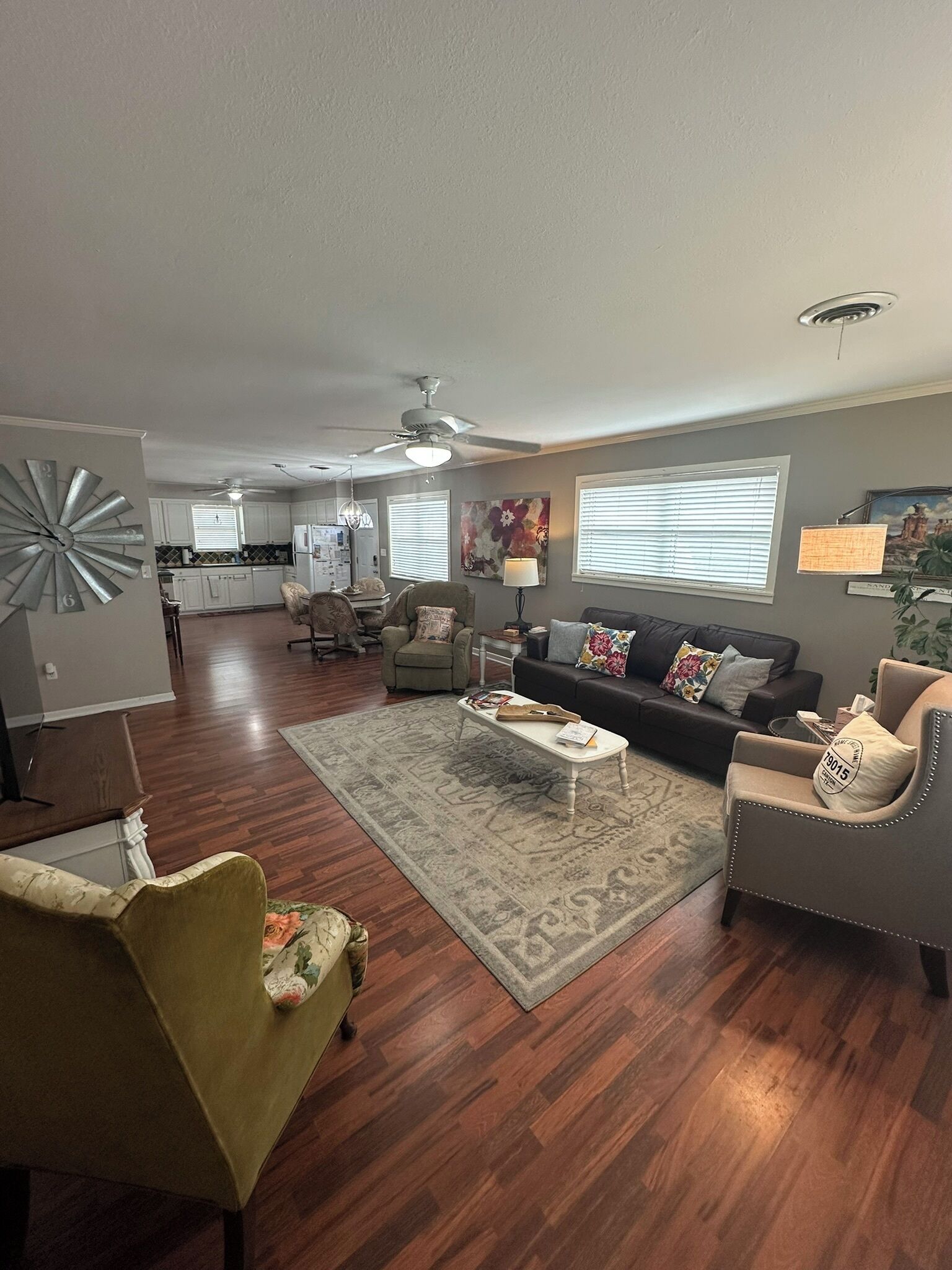 A spacious living room with hardwood flooring, a sofa, armchairs, a coffee table, and a dining area in the background.