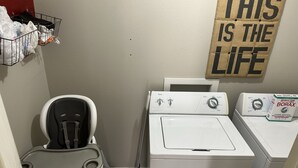 Ett tvättrum med tvättmaskin, torktumlare och en mopp. På väggen finns en skylt med texten: ”DET HÄR ÄR LIVET”.