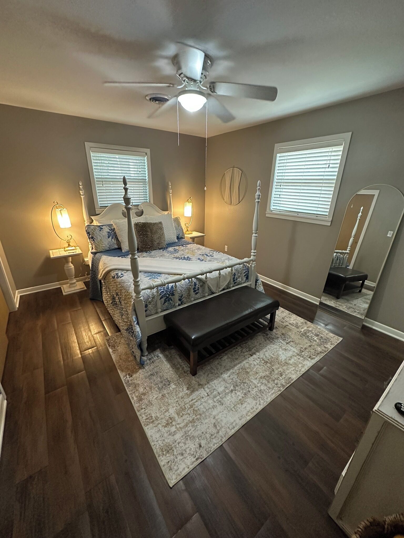 Une chambre à coucher avec un lit, des lampes de chevet, un ventilateur de plafond et un grand miroir.