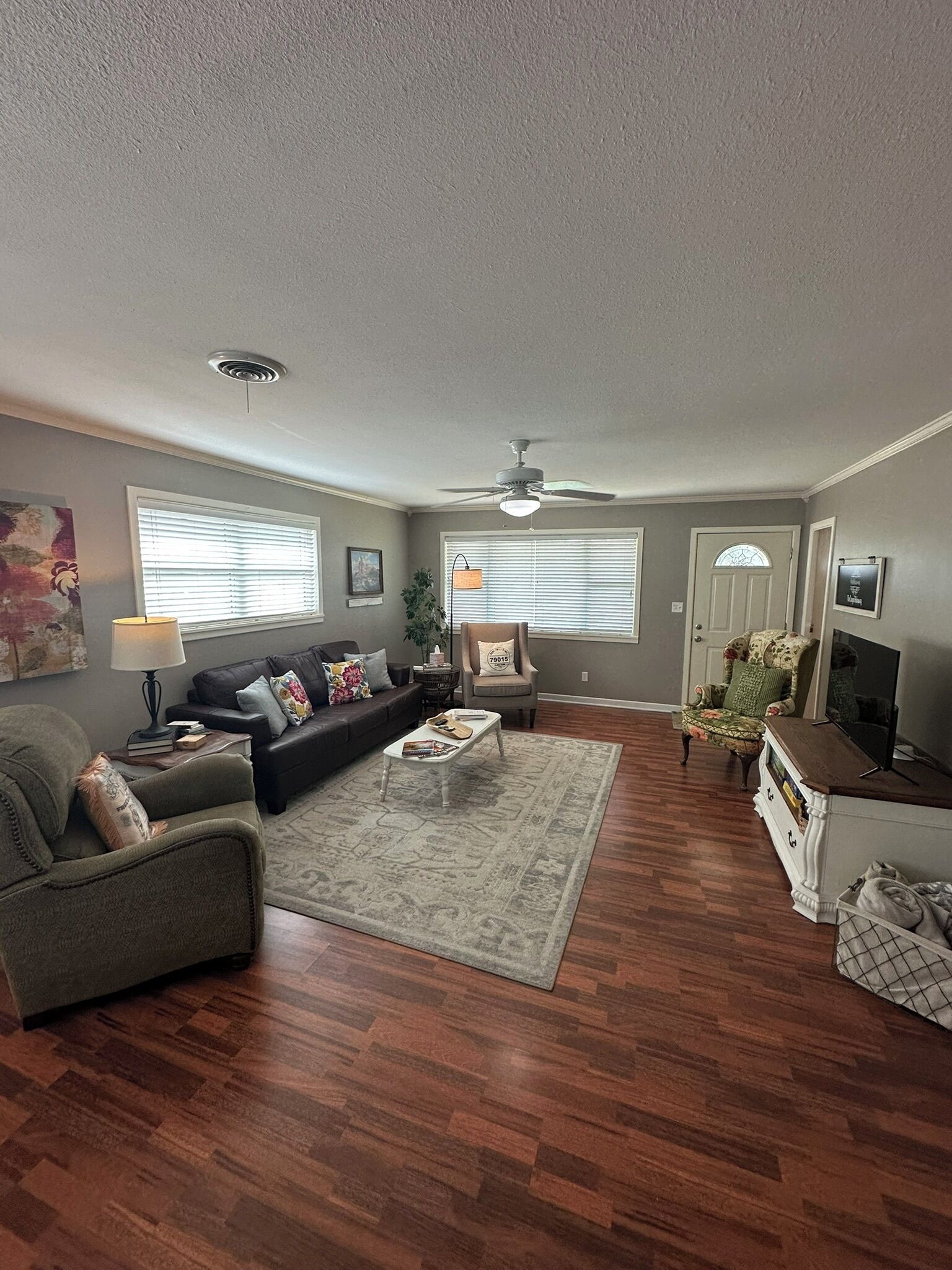 Ein Wohnzimmer mit grauem Sofa, einem Couchtisch, einem gemusterten Teppich und einem Fernseher auf einem Standfuß.