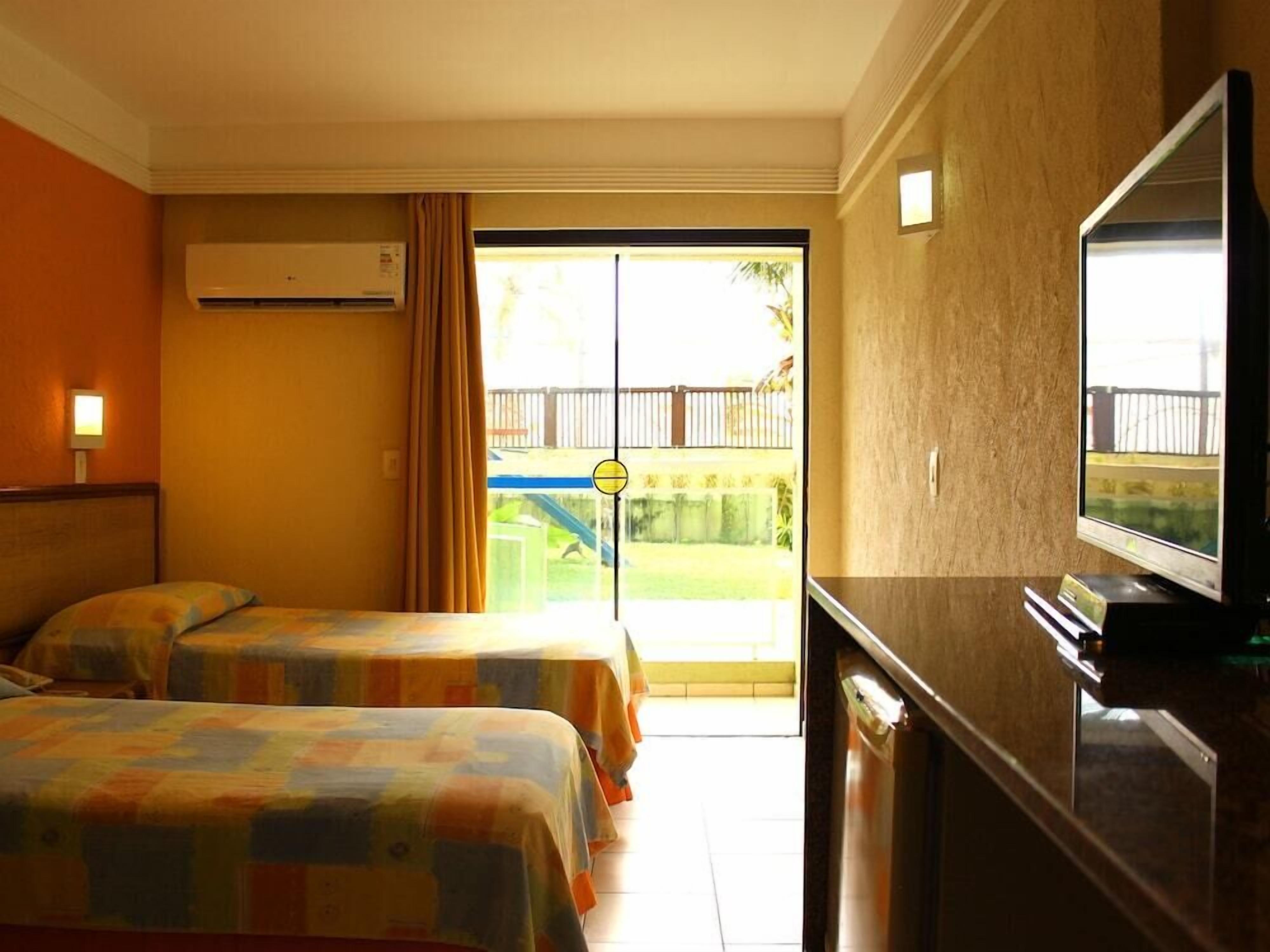 Habitación de hotel con dos camas, televisión, aire acondicionado y puerta corrediza de vidrio que da a un balcón.