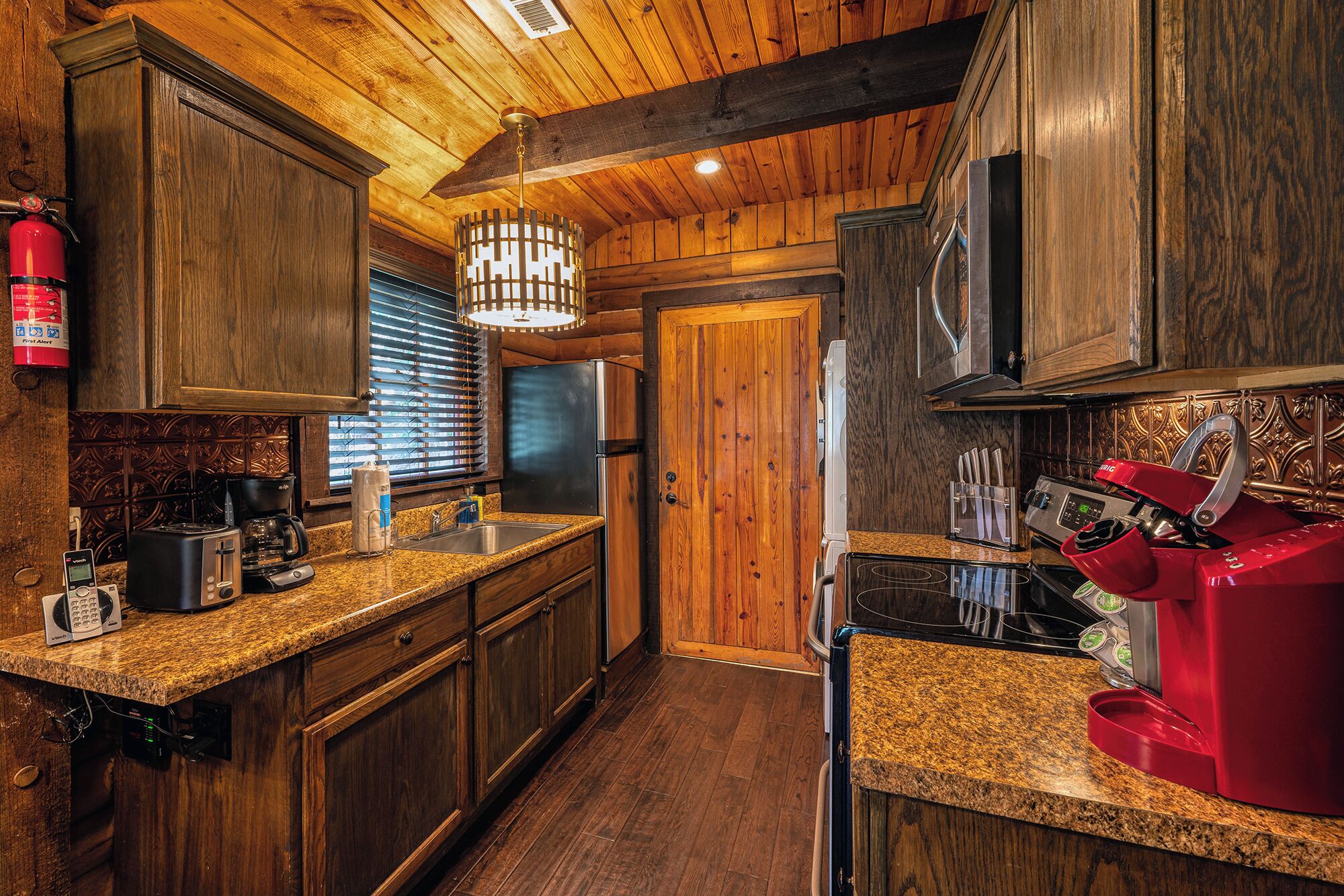 A kitchen with wooden cabinets, a stainless steel sink, a coffee maker, and a red espresso machine.