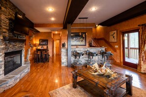 A spacious living room with a stone fireplace, wooden flooring, and a rustic bar area with stools.