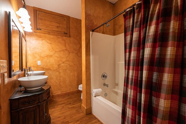 Une salle de bain avec un meuble-lavabo en bois, un évier, un miroir, une douche avec un rideau à carreaux et une porte en bois.