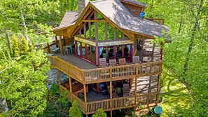 Une cabane en bois à plusieurs niveaux, dotée d’une terrasse et entourée d’une forêt dense.
