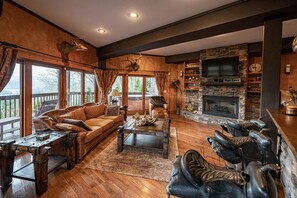 A cozy cabin interior with a stone fireplace, leather furniture, and a large TV.