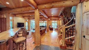A spacious log cabin interior with a large dining area, a living room, and a staircase.