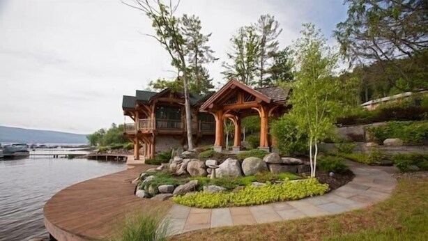 A lakeside cabin with a wooden deck, a stone pathway, and a rock garden.