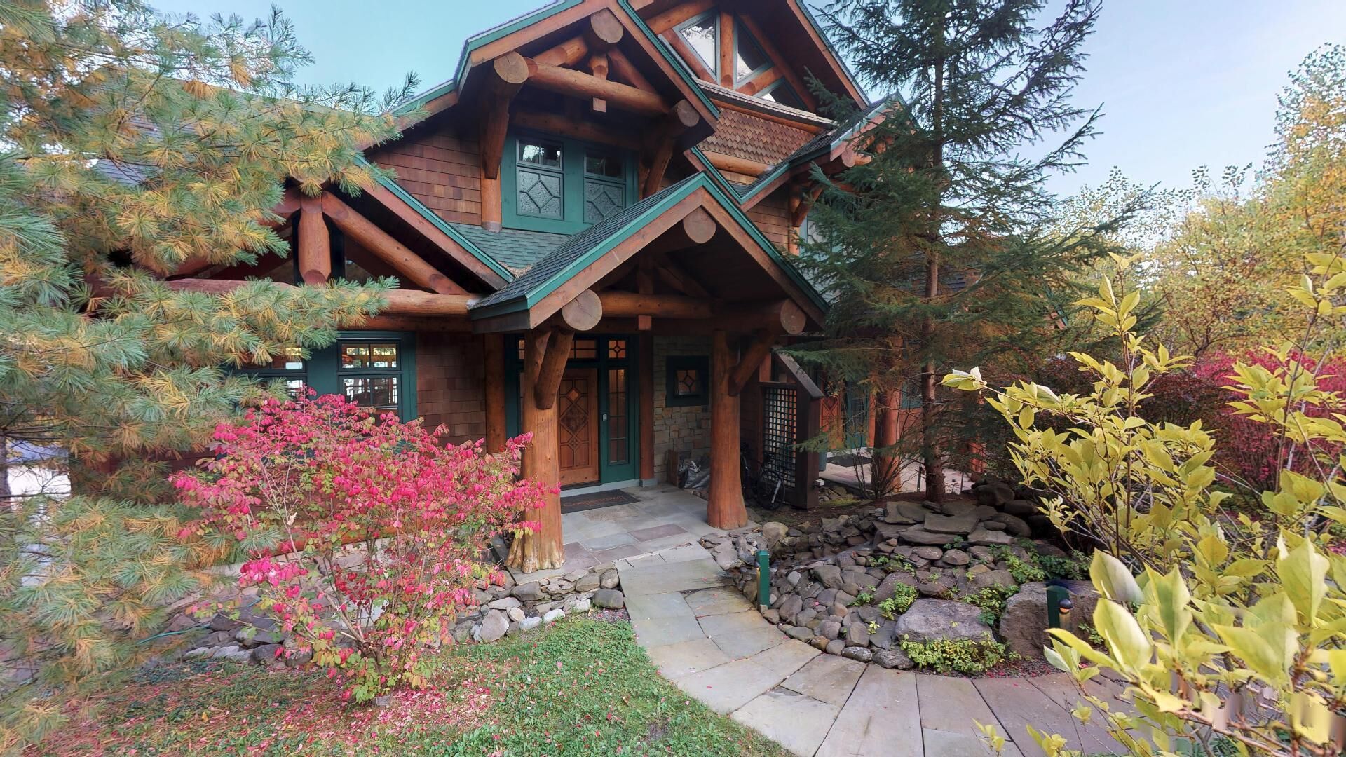 A log cabin with a stone pathway leading to the entrance, surrounded by various plants and trees.