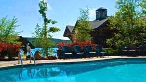 A swimming pool with a stone building in the background, surrounded by trees and outdoor seating.