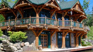 A log cabin with a stone foundation, wooden balconies, and a pond in front.