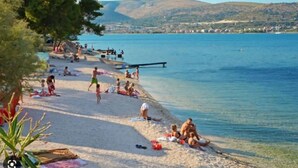 A beach with people sunbathing and swimming, a pier extending into the water, and hills in the background. - Apt Tina, Modern, 2 bedrooms, Outdoor Space & BBQ, close to beach (Mastrinka)