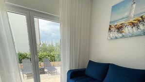 A living room with a blue sofa, a glass coffee table with a cityscape design, and a painting of a lighthouse on the wall. - Apt Tina, Modern, 2 bedrooms, Outdoor Space & BBQ, close to beach (Mastrinka)