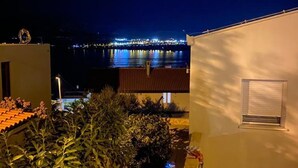 A nighttime view of a coastal area with a lit bridge and a building with a window and a small balcony. - Apt Tina, Modern, 2 bedrooms, Outdoor Space & BBQ, close to beach (Mastrinka)