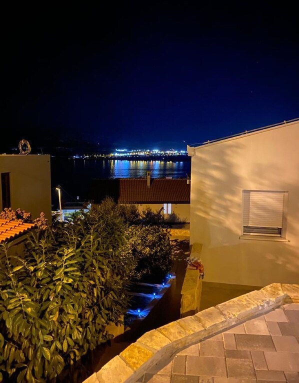 Une vue nocturne d’une zone côtière, avec un pont illuminé et un bâtiment doté d’une fenêtre et d’un petit balcon.