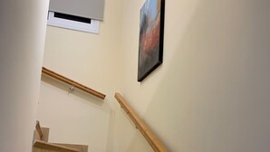 Eine Treppe mit hölzernen Geländern und beigefarbenen Stufen, die zu einer Zwischenebene mit weißer Decke und einer Leuchte führt.